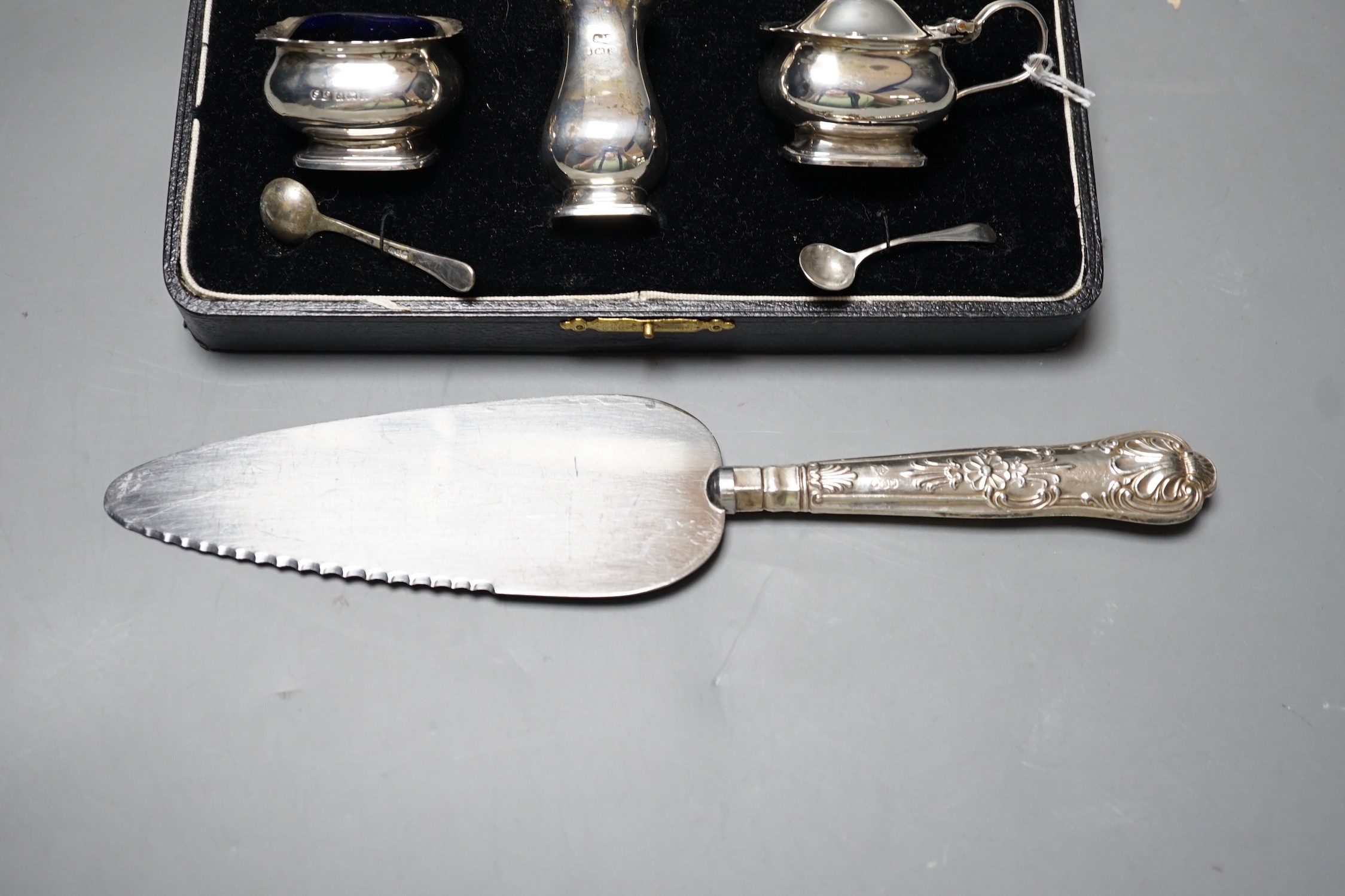 A cased George V silver three piece condiment set, Birmingham, 1930, a Victorian engraved silver snuff box, a pair of silver mounted dwarf candlesticks and a silver handled cake slice.
